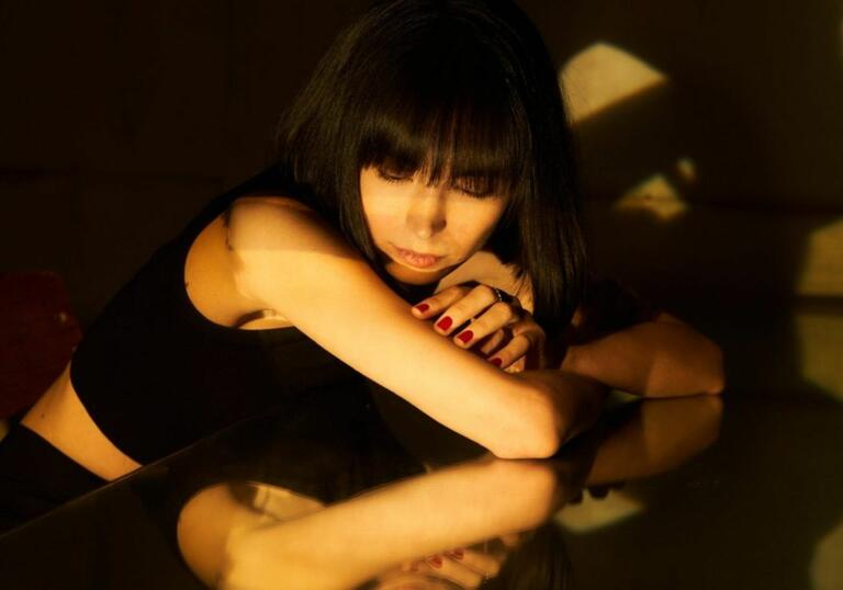 Pianist Alice Sara Ott leaning on the piano, her reflection is visible on the instrument.