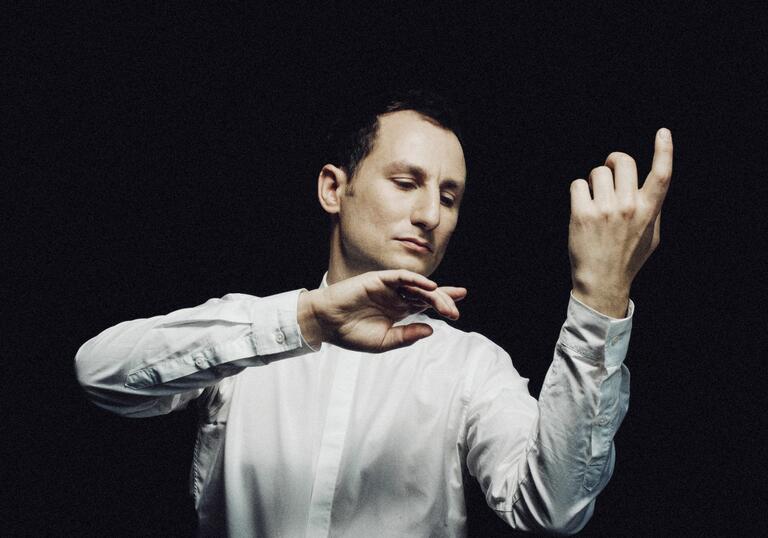 Violist Antoine Tamestit in front of a black background imitating playing his instrument without the actual instrument being there. His eyes are closed.