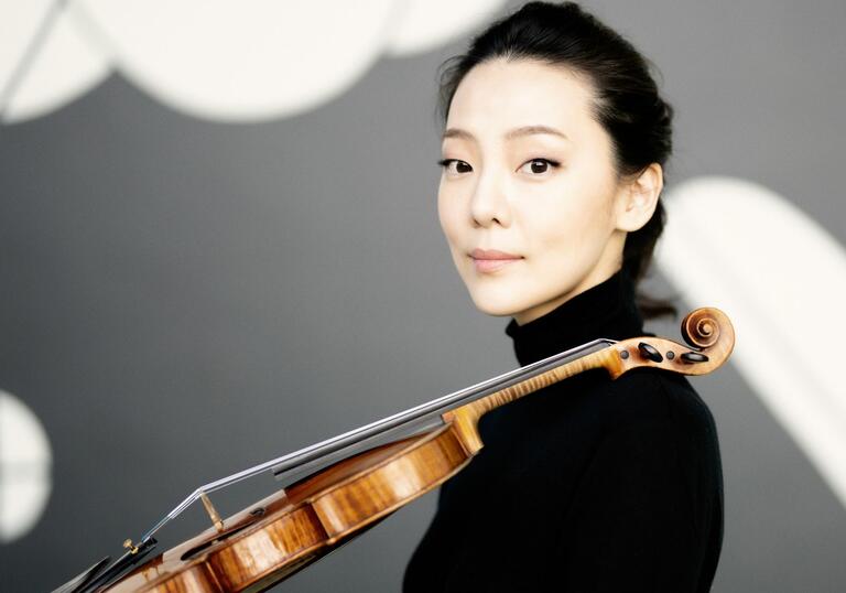 Violinist Clara-Jumi Kang resting her violin in her shoulder while looking into the camera