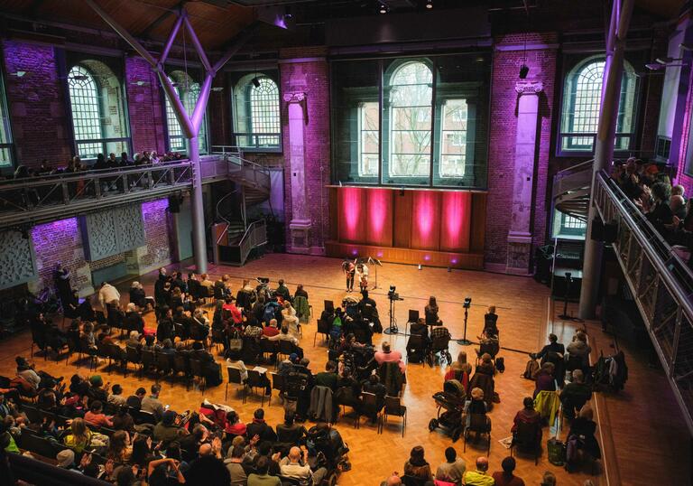 A view from the balcony at the back of the Jerwood Hall in LSO St Luke's, showing the audience sat in chairs and two musicians bowing on-stage