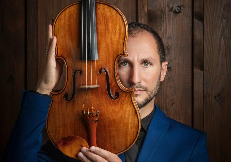 Antoine Tamestit facing the camera, holding a viola upright and facing forwards, in front of the side of his face