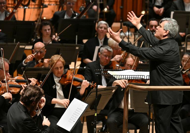 Sir Antonio Pappano conducting the London Symphony Orchestra, facing the Orchestra on the conductor's podium, with both hands raised in the air
