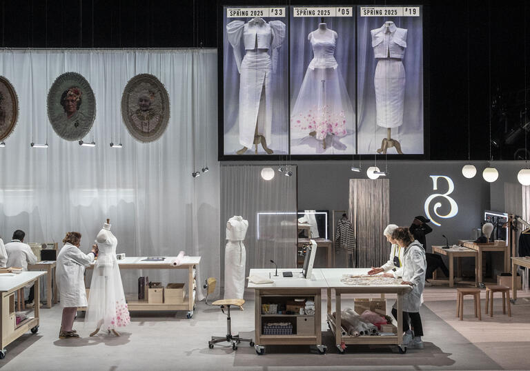 Set image of a room full of people working together to create a dress. The room contains 