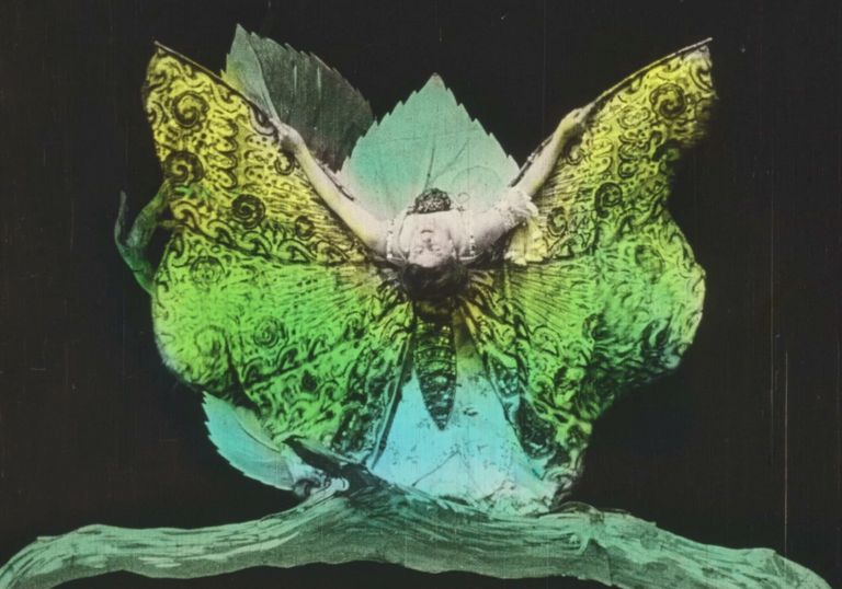 A woman dressed as a butterfly, blue, green, yellow, bends backwards towards the camera
