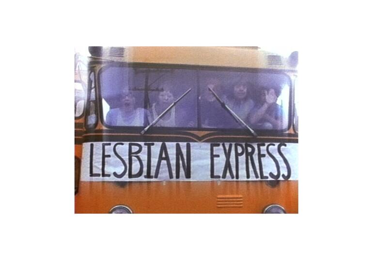A still from Superdyke, showing the front of a bus with a group of women inside. On the front of the bus is a large banner saying Lesbian Express.