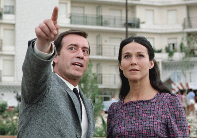A male-presenting character stands on the left, pointing at something ahead of them. A woman stands on the right, her gaze following his finger.