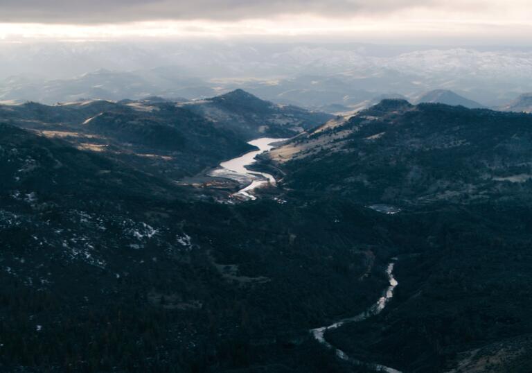 A mountainous landscape, with a reservoir and dam in the foreground and a river winding through the hills beyond.