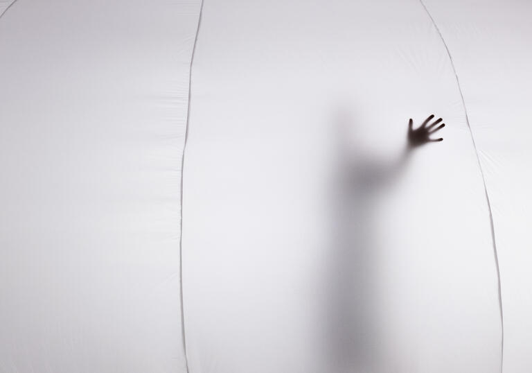 The silhouette of a person can be seen from inside a bubble, their hand is pressed against the material.