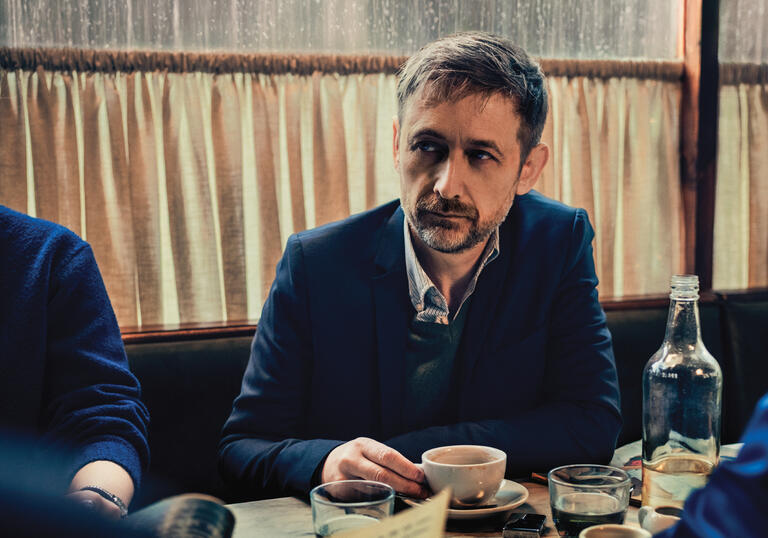 Neil Hannon sitting at a table drinking coffee