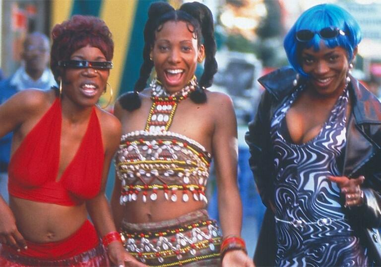 Three Black women standing in a row and smiling, wearing colourful clothes