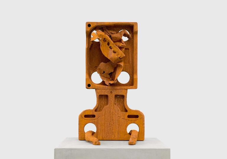 A cast iron sculpture that loosely resembles a head and shoulders, with a twisted form in the head cavity.