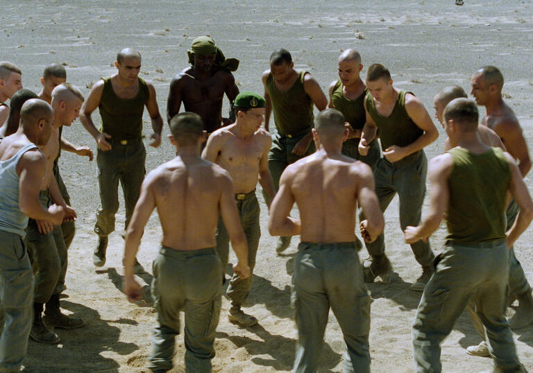 Shirtless men stand in a circle ready to fight