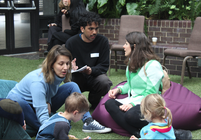 Two women sit with their children as an interviewer asks questions about Renewal in a relaxed setting in the Conservatory