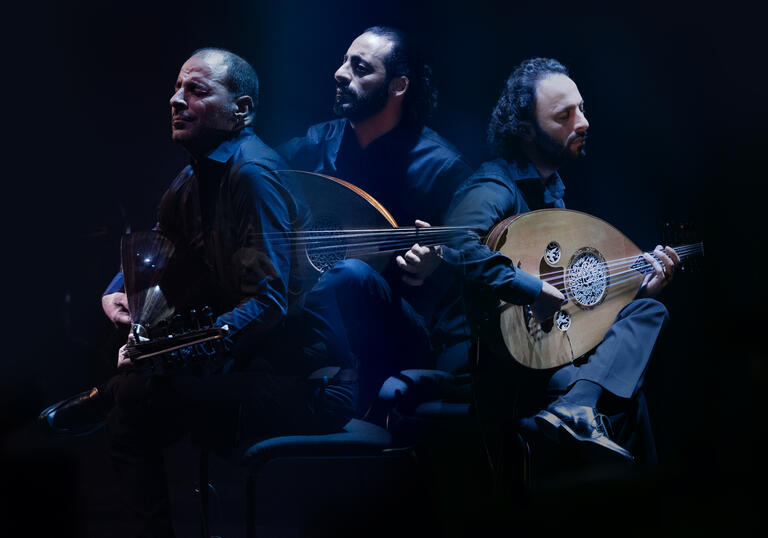 trio playing string instrument and singing in dramatic lighting