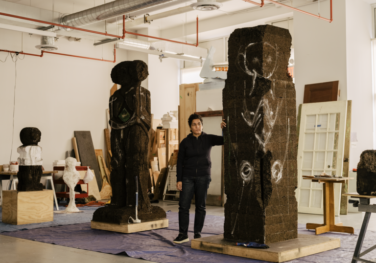 huma bhabha stands in front of tall sculptures