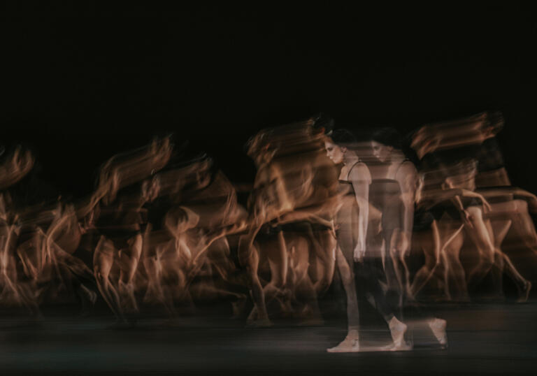 Blurry image of multiple dancers in dark costumes