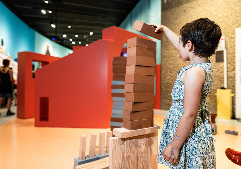A small child plays jenga, they reach to put a block on the top.
