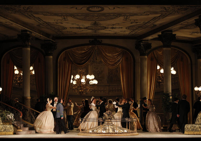 A scene from Arabella showing a group of men and women in 19th-century formal wear, standing in a grand ballroom