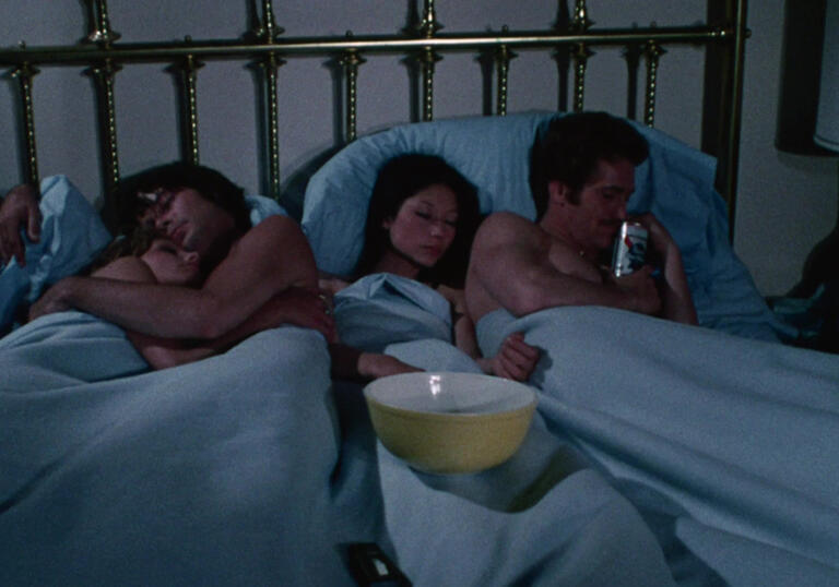 Two couples lie in bed together.