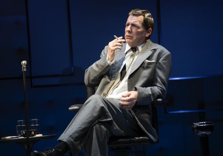 Sean Hayes is Oscar Levant, he sits and looks concerned in a talk show chair.