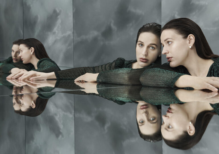 A brunette woman stars at her own reflection, repeated multiple times