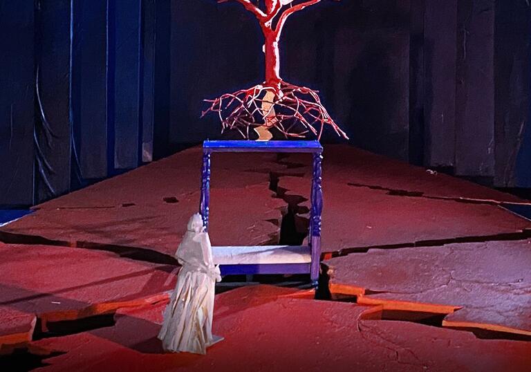 A figure standing in front of a towering, red tree-like structure