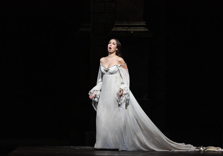 A woman in a white dress sings on a stage.