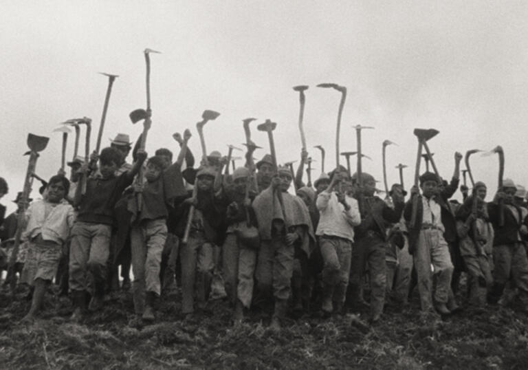 A group of people with land tools walk in a line.