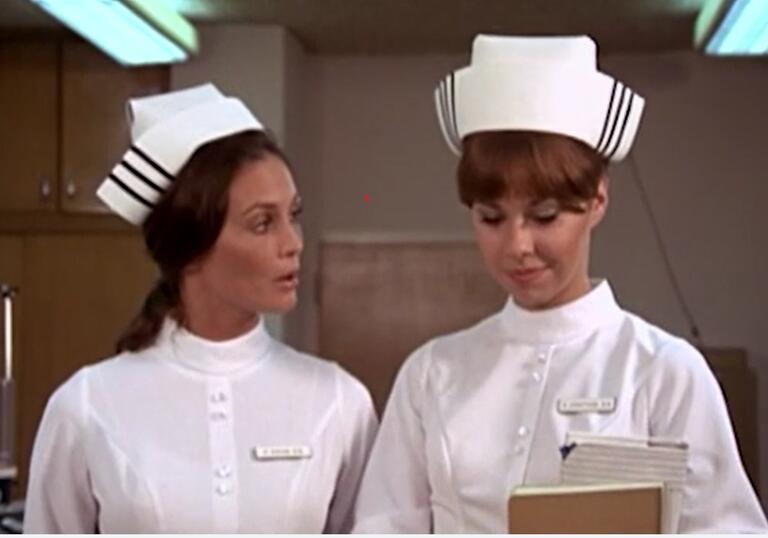 Two student nurses walk down a corridor of a hospital.