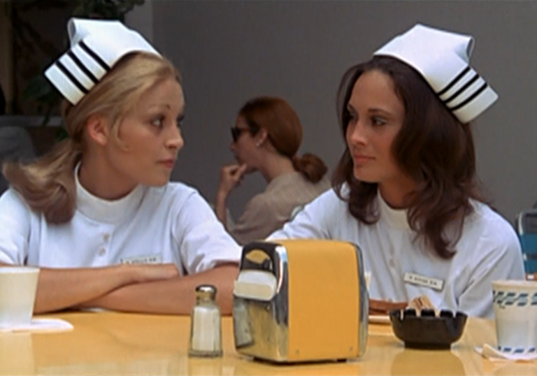 Two young student nurses sit at a lunch table.