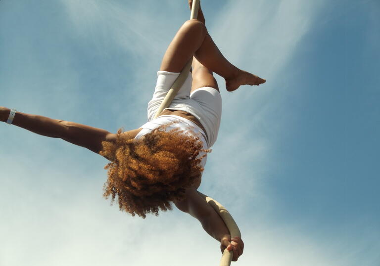 A person performing an aerial act hanging upside down from a rope