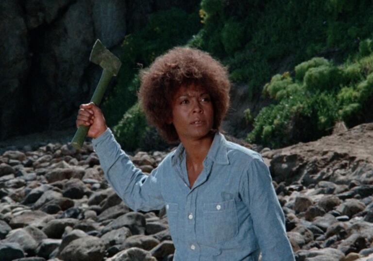A woman wields a knife on a beach.