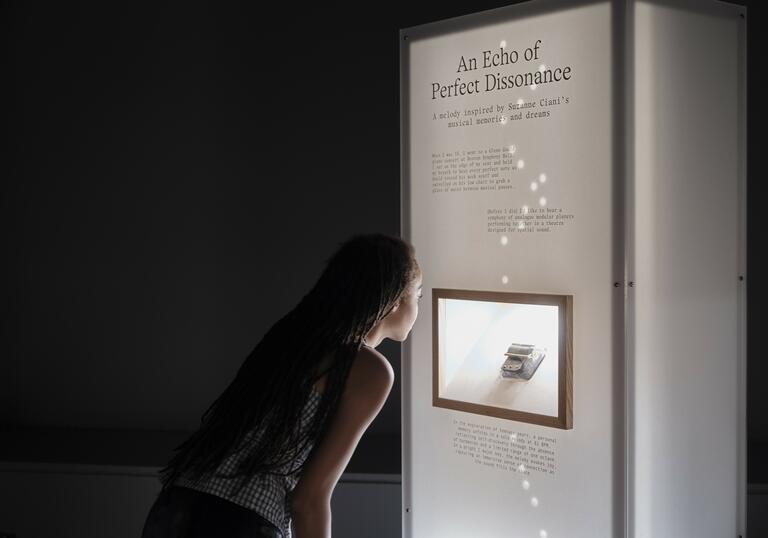 A woman leans in to look at a music box mounted in an illuminated pillar