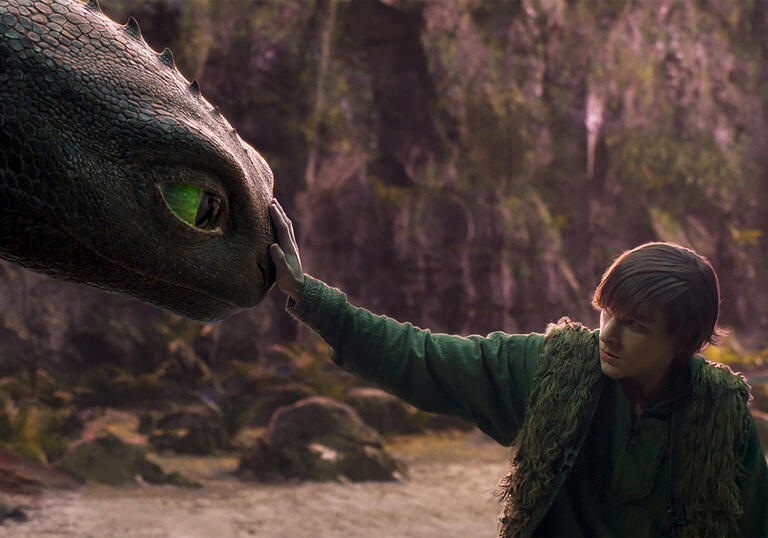 A black dragon is touched on the nose by a young man with brown hair
