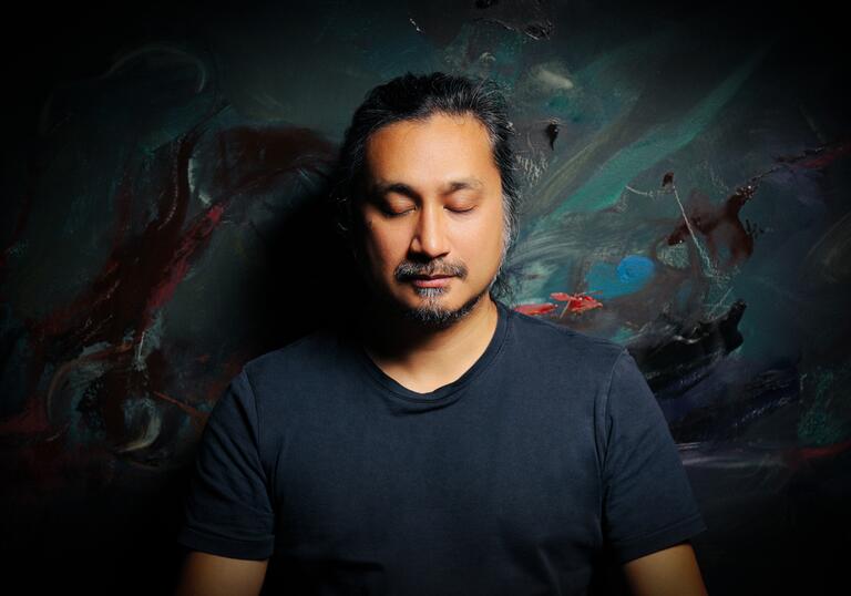 Headshot of an Asian man against a dim colourful background