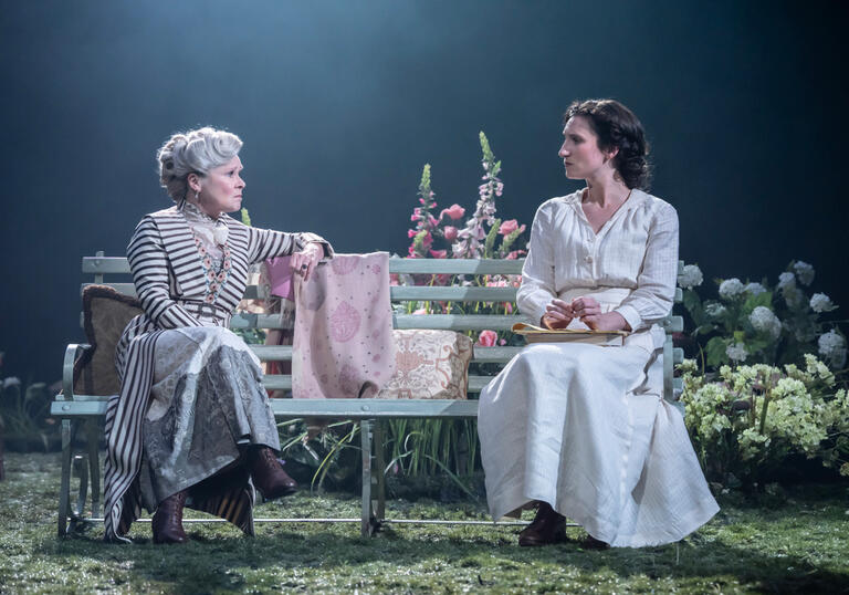 Two women sit on a bench looking at each other