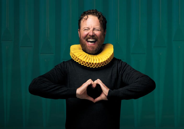 A person with a yellow collar around their neck makes a love heart symbol with their hands.
