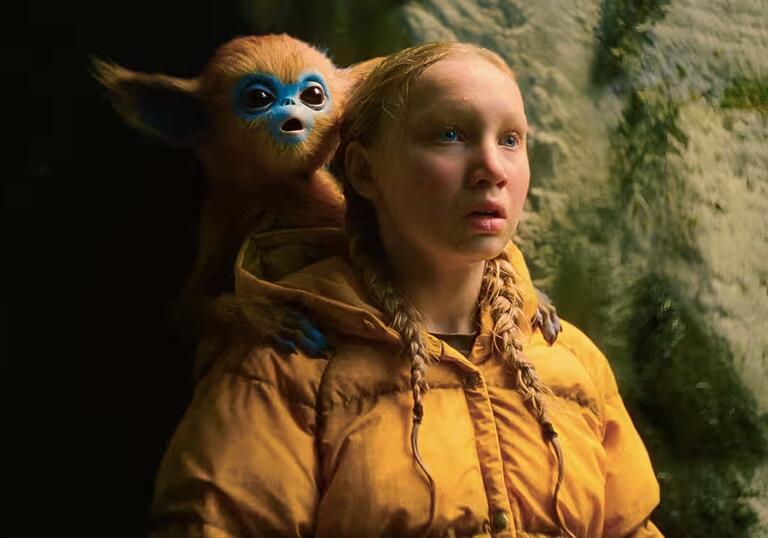 A young girl wearing a yellow puffer coat has a fantastical creature on her shoulder