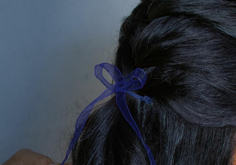 Close up of the back of head of a girl or woman with dark hair, tied with a blue bow