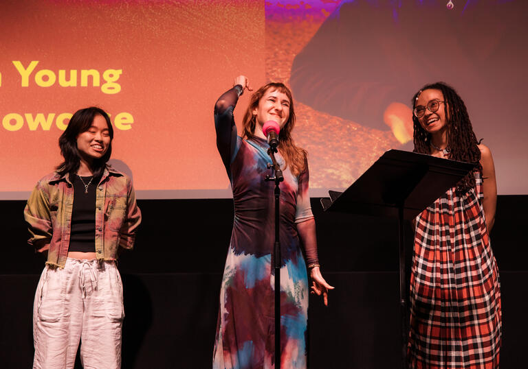 Three women stand on a stage performing