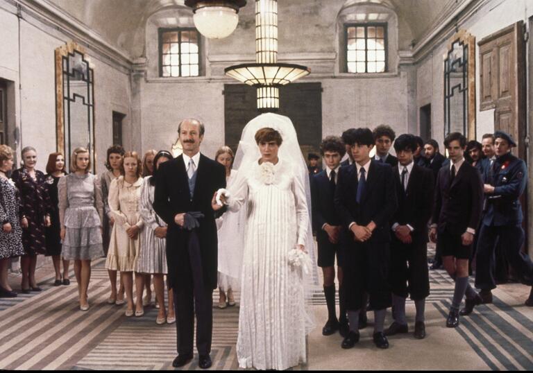 A man and a woman dressed in wedding attire with people standing behind them.