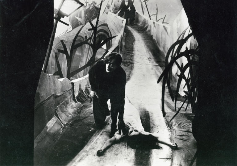A man in a distorted walkway with a woman lying on the floor.