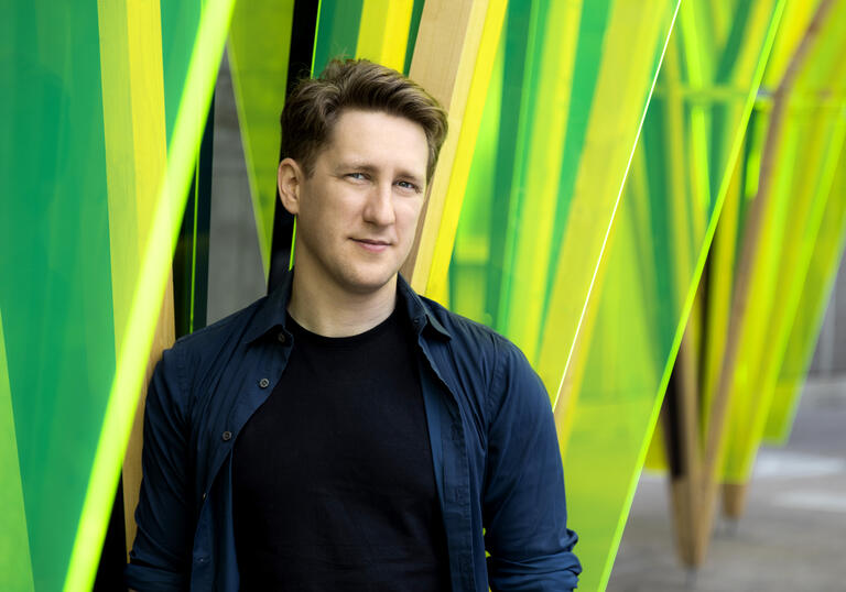 Conductor Joshua Weilerstein standing in front of vibrant green background