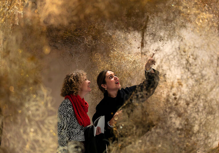 Two women examining a large art installation, displaying expressions of curiosity and interest.