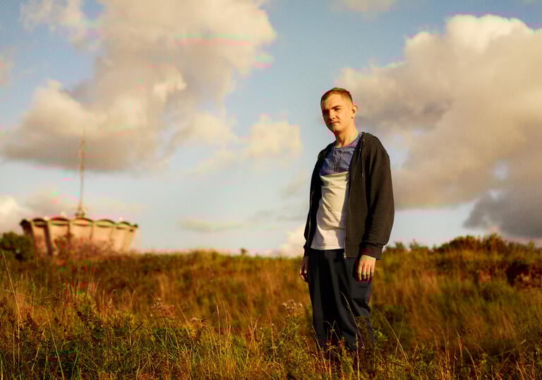 A young white man stands in a field looking into the sunset