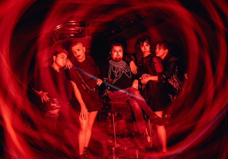 The creative team of Transpose pose alongside each other against an iconic Barbican backdrop with a red swirling light around them.