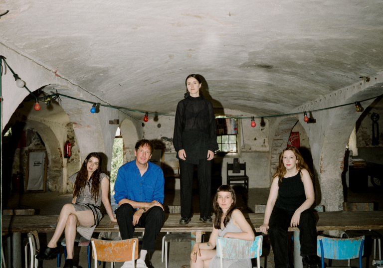 An image of Christian Loffler and band mates sat at a table in a rustic looking room