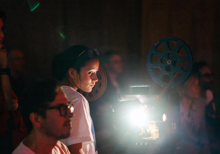 A group of people and a young child look on. A film projector emits light