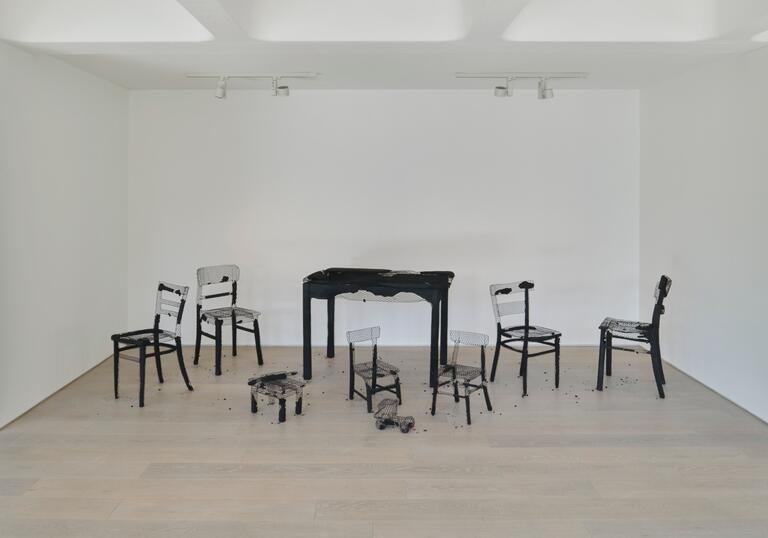 A set of tables and chairs, all burnt out and their charred remains revealing their chicken wire frames.