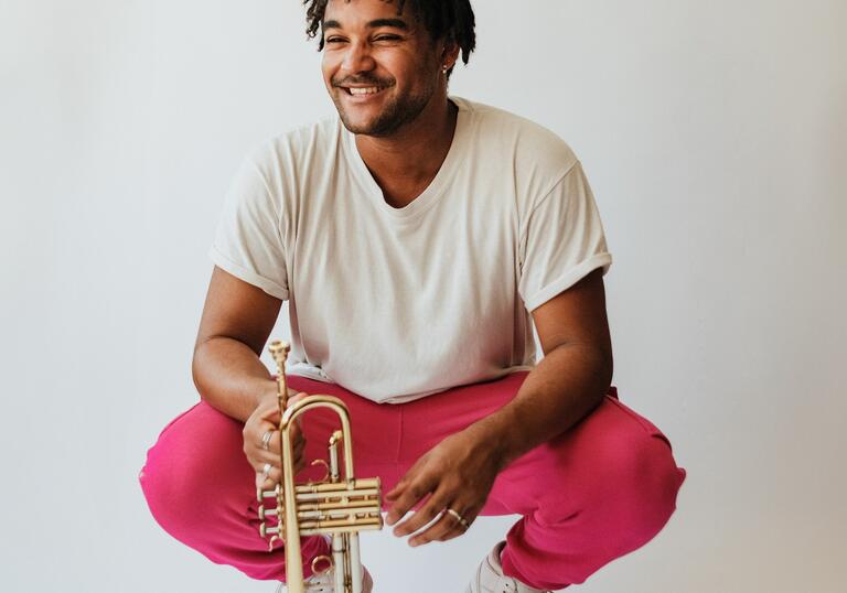 Aaron Akugbo crouching while holding a trumpet